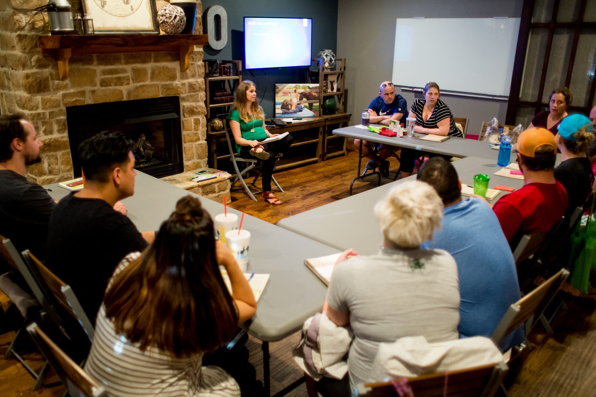 Couples attending an in-person childbirth class with instructor leading discussion in a classroom setting.