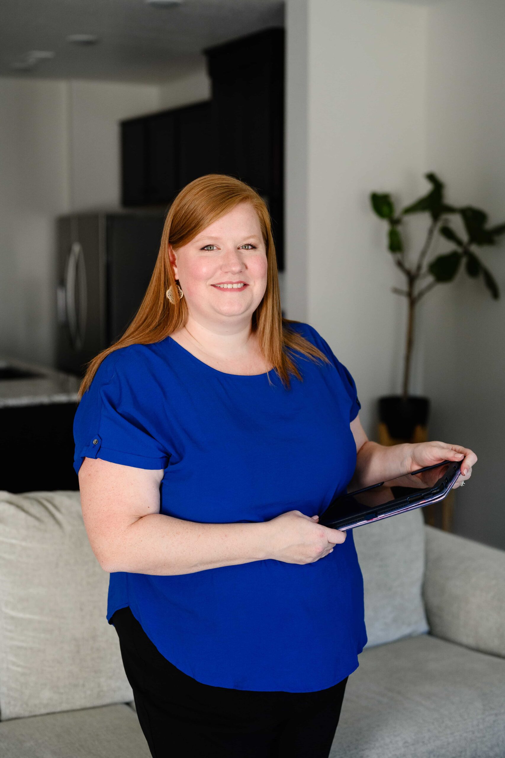Hollie Hauptly, a Utah based childbirth educator and doula, is holding a tablet while she teaches her childbirth classes in a living room.