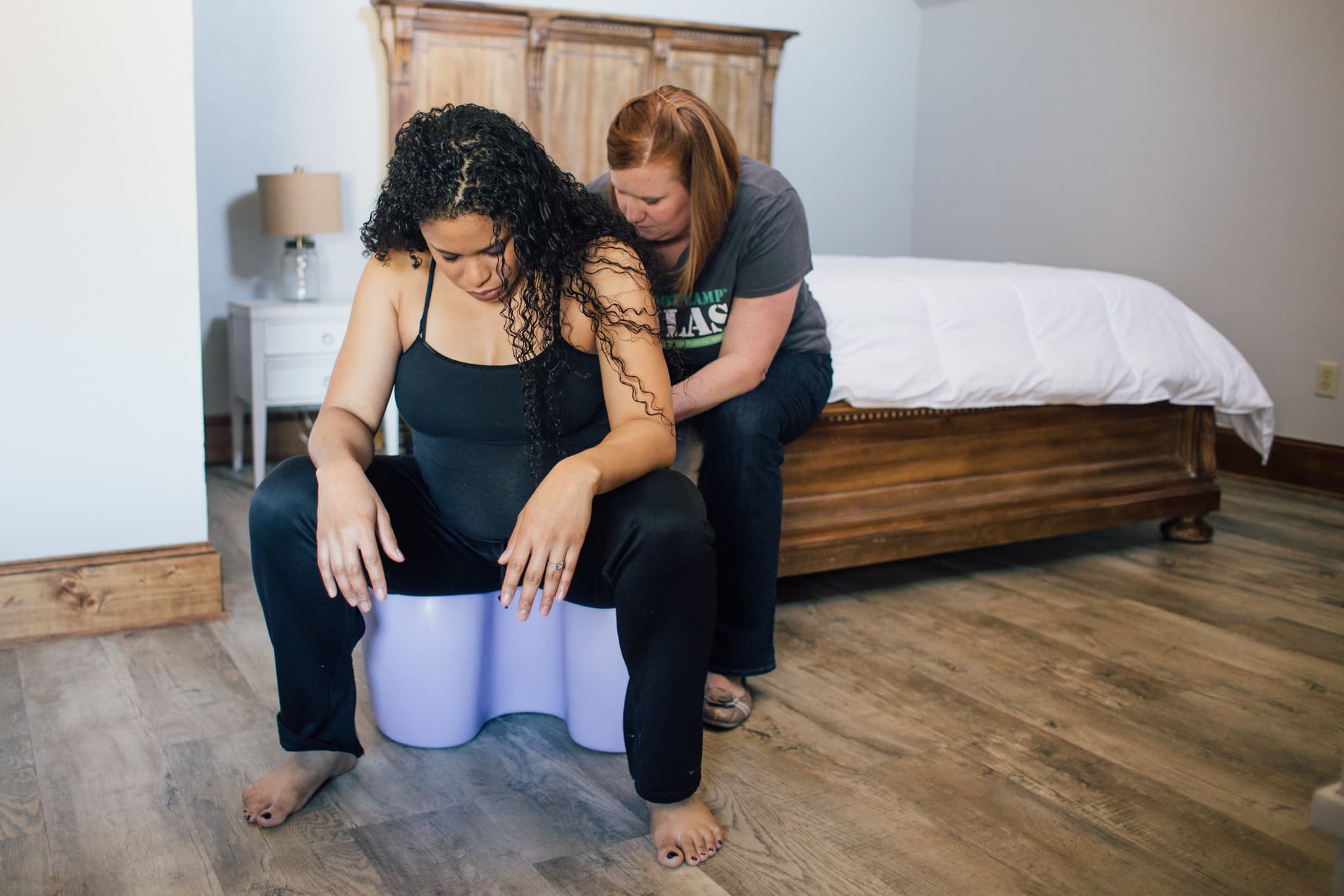 Doula providing hands-on labor support to a pregnant woman practicing birth positions using a birth stool.